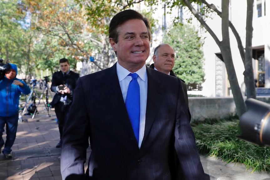 Manafort walks down footpath followed by media