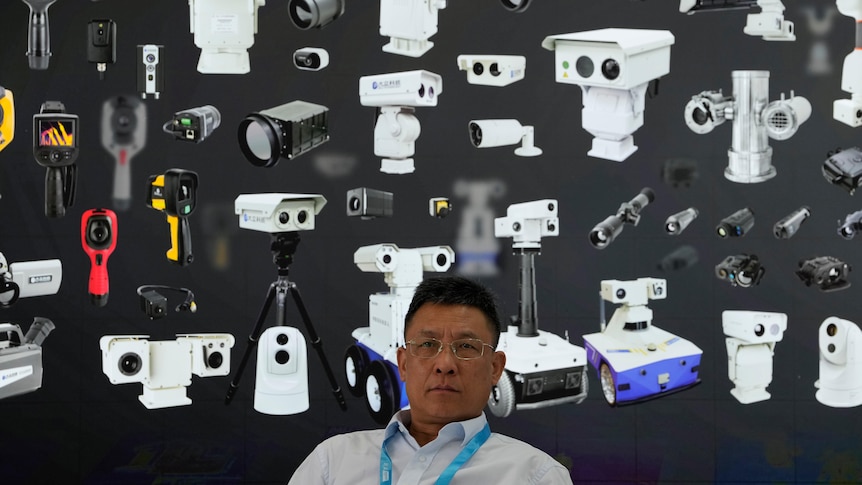 A vendor sits near a board depicting surveillance cameras during Security China 2023 in Beijing.