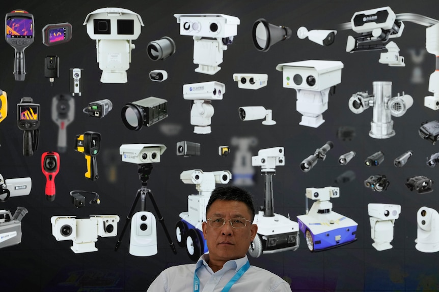 A vendor sits near a board depicting surveillance cameras during Security China 2023 in Beijing.