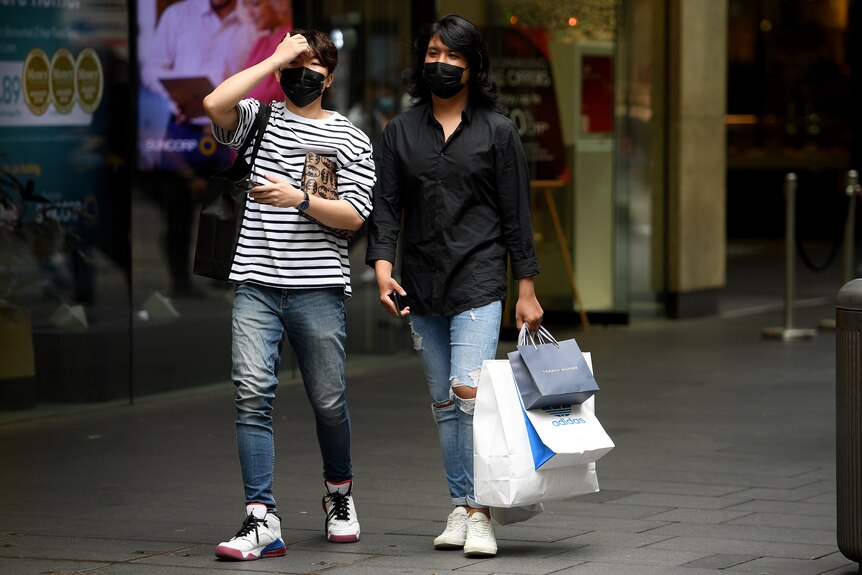 a young man wearing a covering over his mouth walks with another man wearing a covering over his mouth