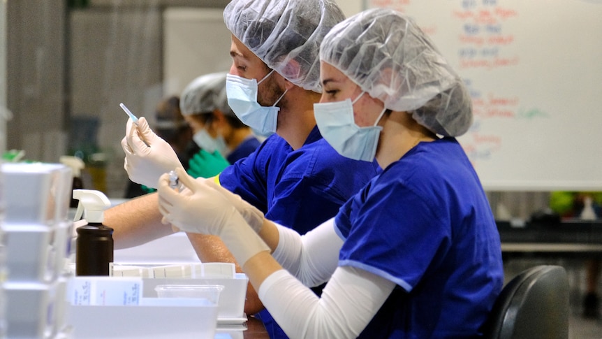 Health workers wearing personal protective gear as they prepare COVID vaccinations