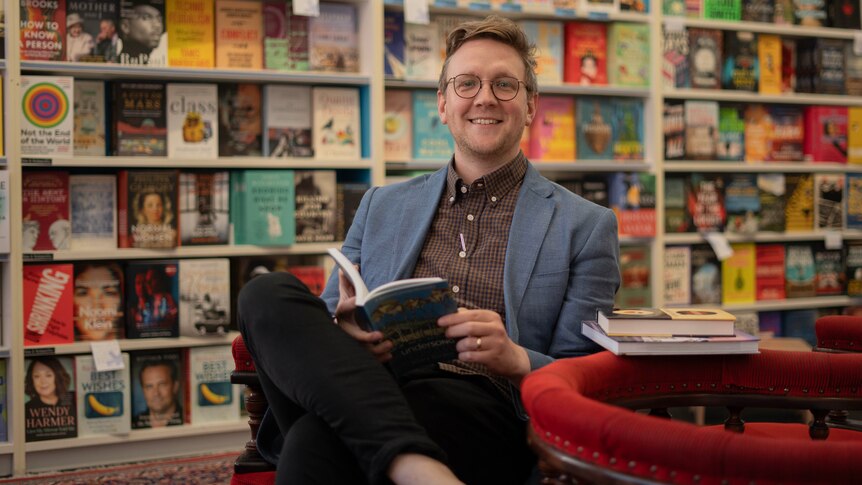 A man smiles at the camera in a bookstore.