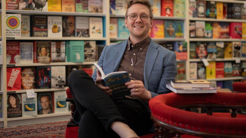 A man smiles at the camera in a bookstore.