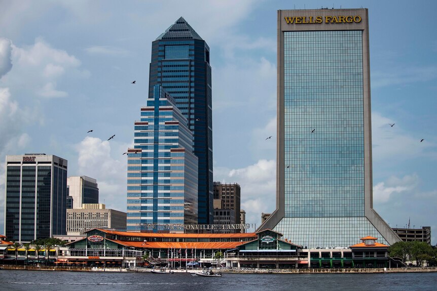 View from the water of a low-set dining and enertainment precinct, with signs saying Jacksonville Landing, with two skyscrapers
