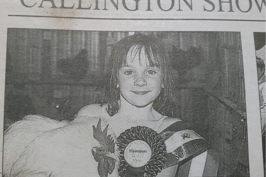 Une jeune fille tient un poulet avec un ruban gagnant.