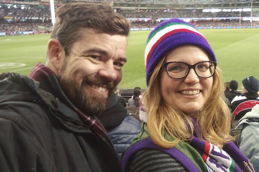 Tim Hall et sa femme prennent un selfie souriant dans la foule lors d'un match sportif. 