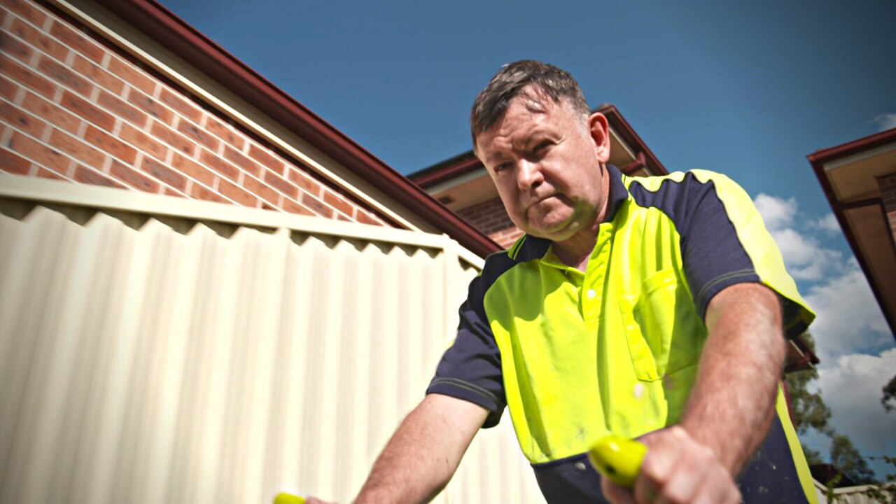 Man wearing hi-vis shirt mowing the lawn outside.