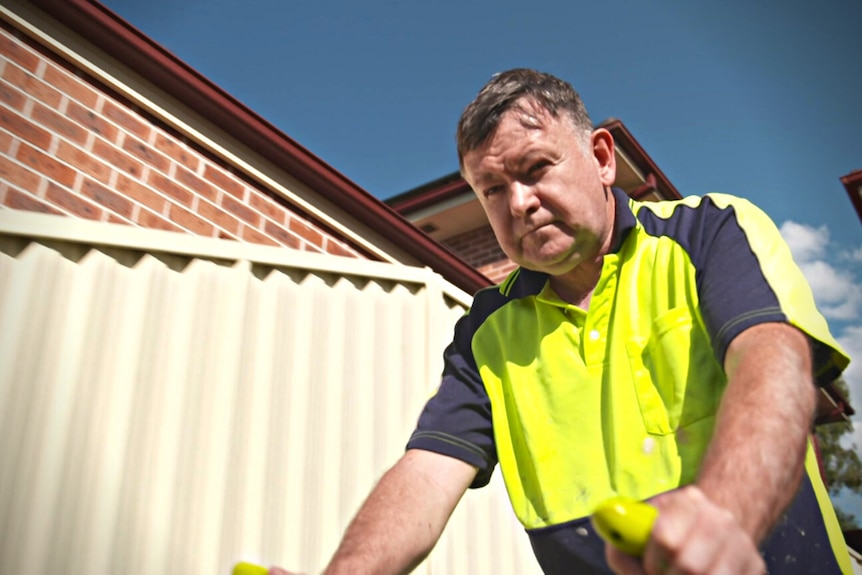 Man wearing hi-vis shirt mowing the lawn outside.