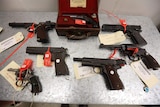 Several pistols laid out on a table with tags on them