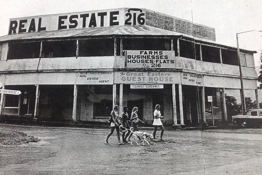 A black and white photos of four young women walking a Dalmatian in front of a rundown guesthouse