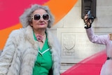 Older woman in big sunglasses with two younger women behind taking a selfie to depict travelling with older people.
