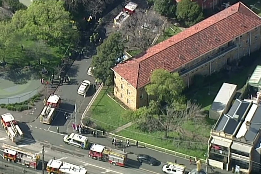 An aerial shot of seven fire trucks parked around a three-story apartment building.