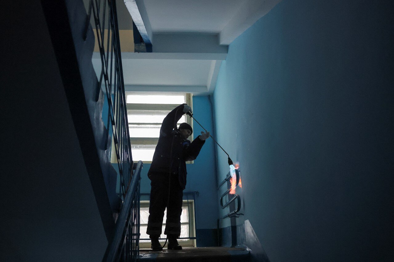 A man using a blowtorch to heat a pipe near a stairway