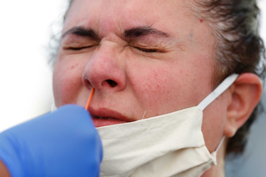 A woman winces with her eyes closed while someone sticks a swab up her nose