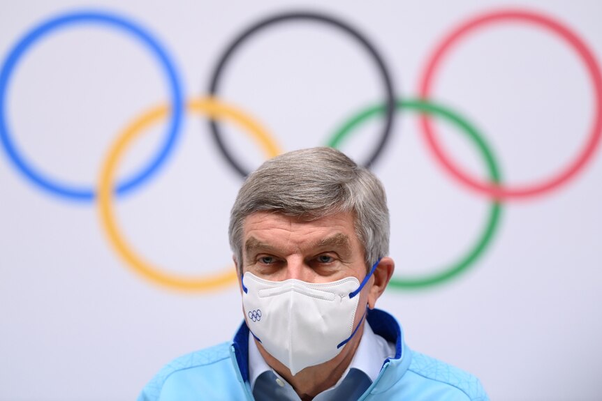 A man wearing a mask sits in front of the Olympic rings
