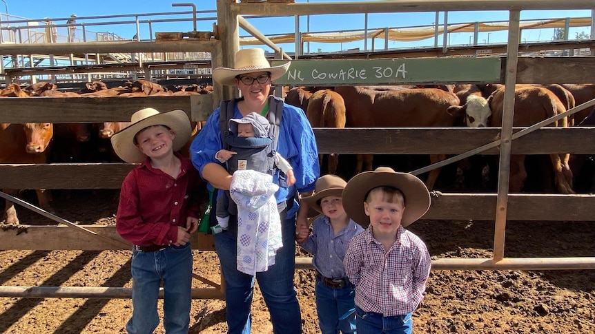 A woman with four young boys smiling standing in front of cattle.