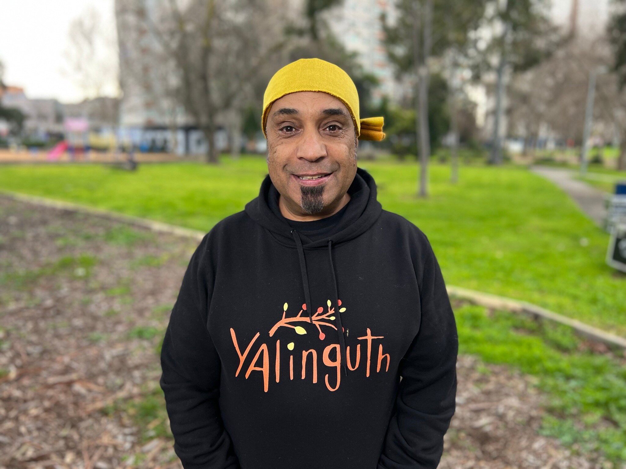 Jason Tamiru smiles, wearing a black hoodie and yellow beanie.