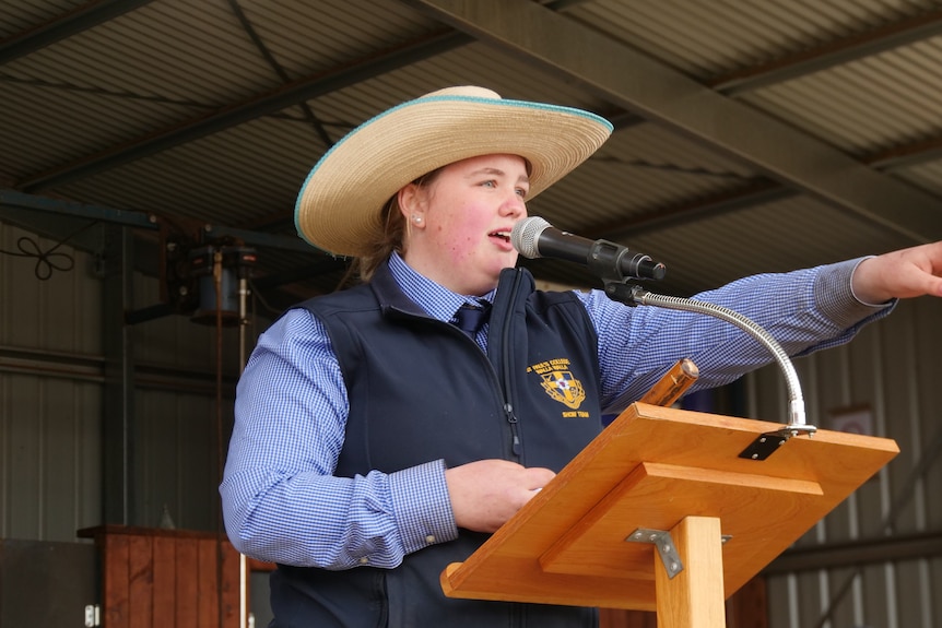 A young woman in a hat, vest and business shirt conducts an auction.