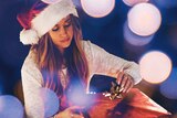 Woman wearing a Santa hat opening a Christmas present on her own to depict what to do when you feel lonely this holiday season.