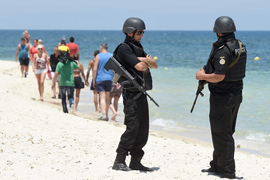 Tunisian policemen patrol the beach as tourists take part in a ceremony on July 3, 2015