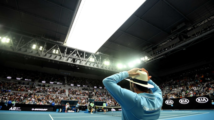 A linesman stands at courtside duri9ng a tennis tournament as the stadium roof begins to close.