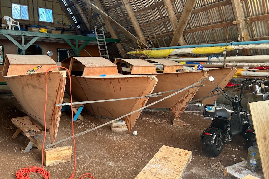 Two double-hulled boats being built in a workshop. So far, their hulls have been shaped from wood