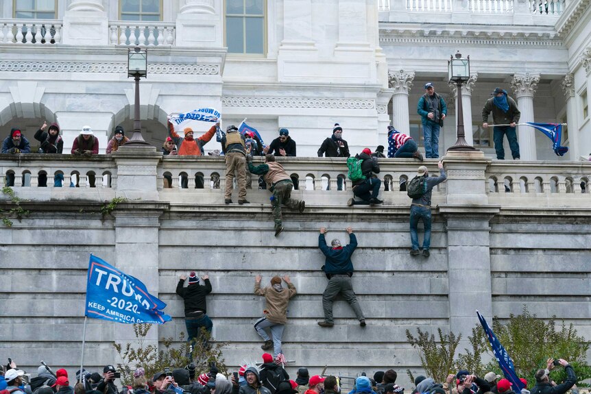 People climbing up a wall leading to the US Capitol building