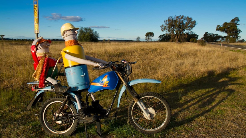 A mailbox made out of a cylinder, resembling a person riding a motorbike with a pillion passenger on the back