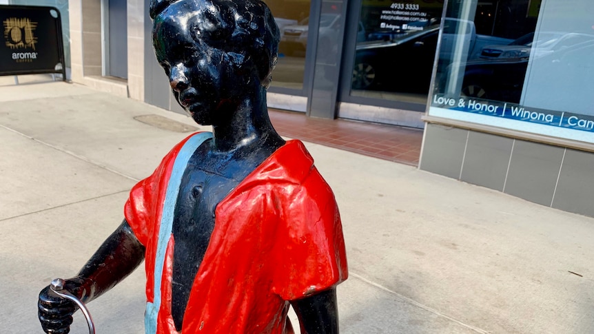 A statue of a black boy dressed in blue shorts and a red shirt 