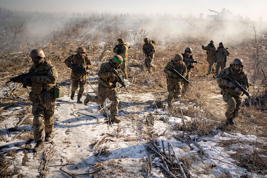 Ten soldiers move across a barren snowy field with rifles raised.
