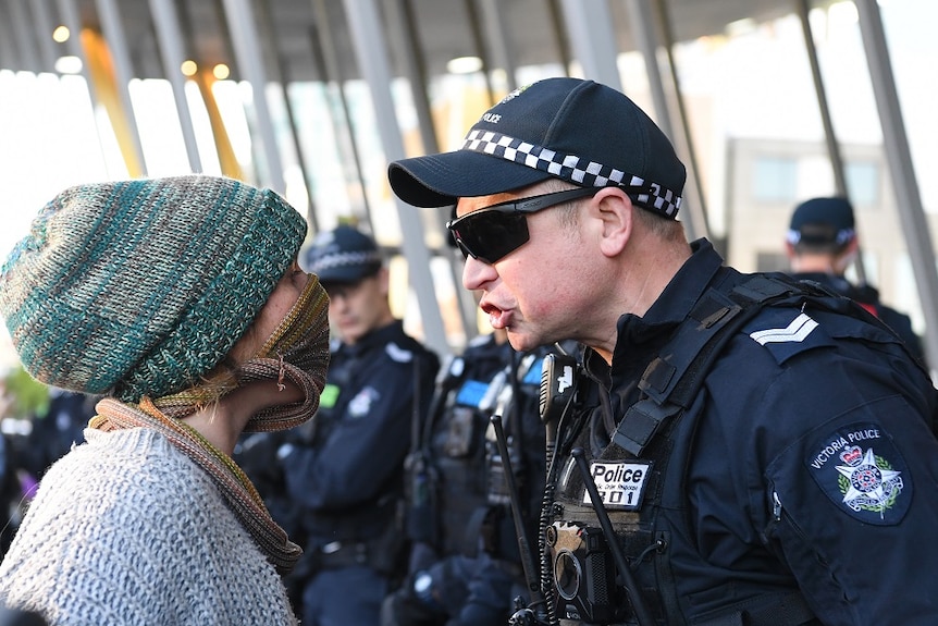 A police officer and protester stand up close, face to face, with the officer shouting at the protester.