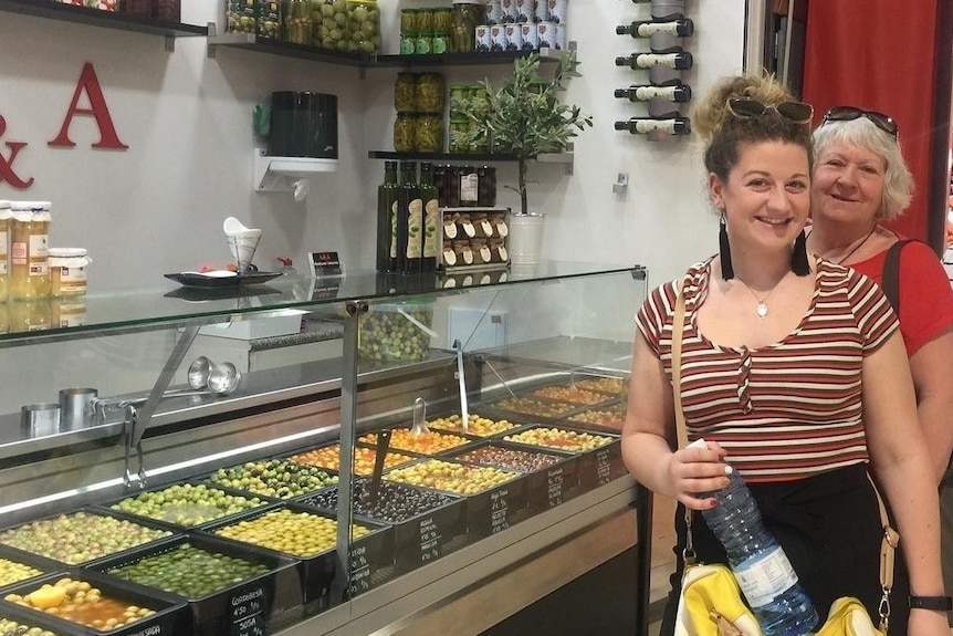 two woman are standing in front of an olive store