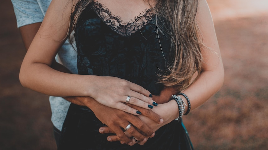 A man is hugging a woman from behind and placing his hands on her belly.