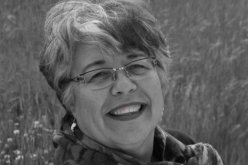 Close-up black and white photo of a woman wearing glasses smiling in a field.