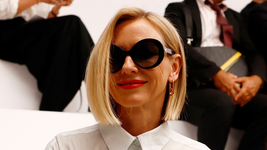 Naomi Watts wearing a white shirt and sunglasses with short blonde hair