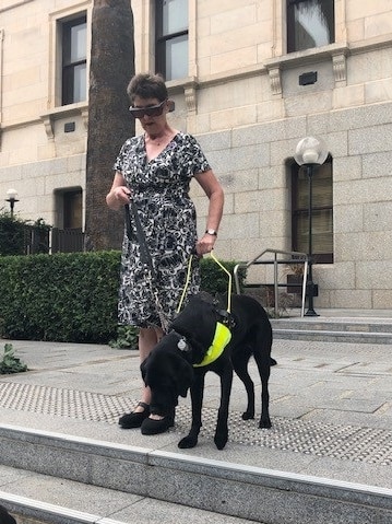 A woman walks down stairs holding onto her black Labrador guide dog Molly