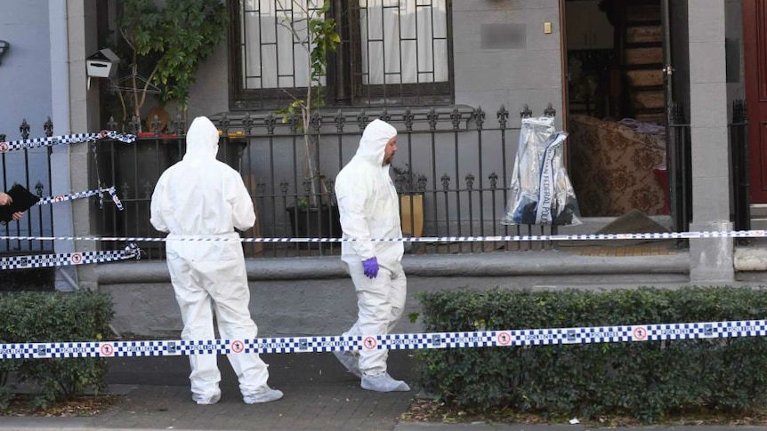 Men in white protective suits stand in front of townhouse in Sydney with police tape.