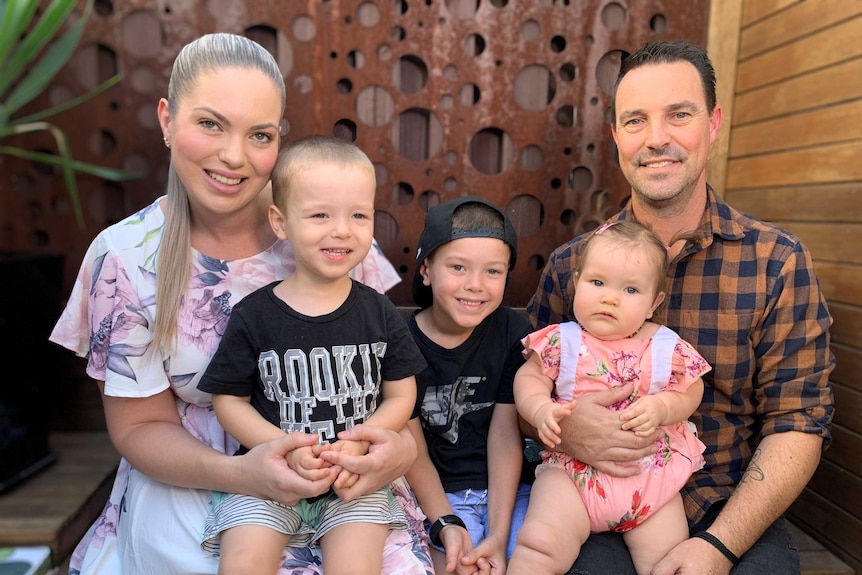 The Stuart family sitting on a wooden bench in front of a rusty metal wall.