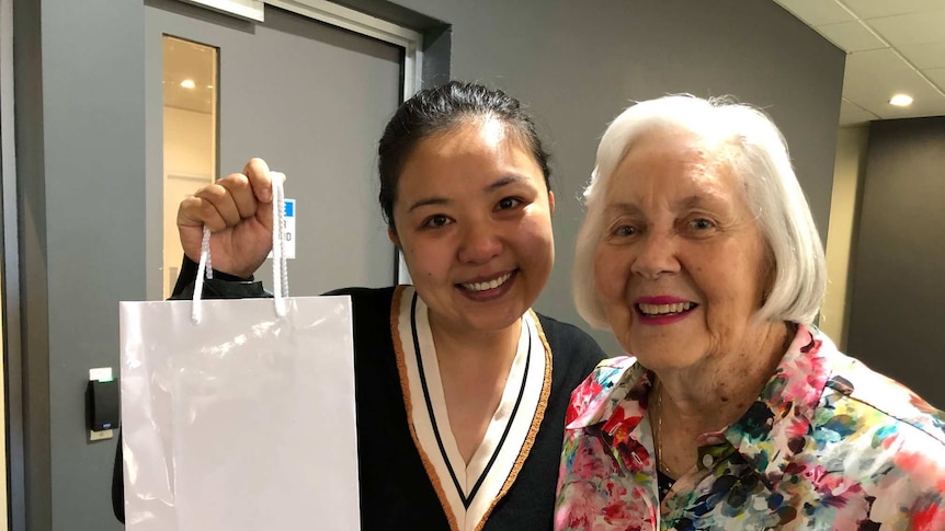 Two ladies smiling and one lady holding a bag