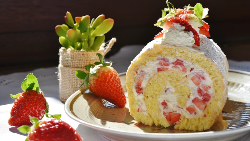 You view a slice of strawberry roulade on a plate with strawberries around the rim.