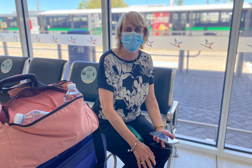 A woman wearing a faecemask sitting down in a bus shelter at Perth Airport.