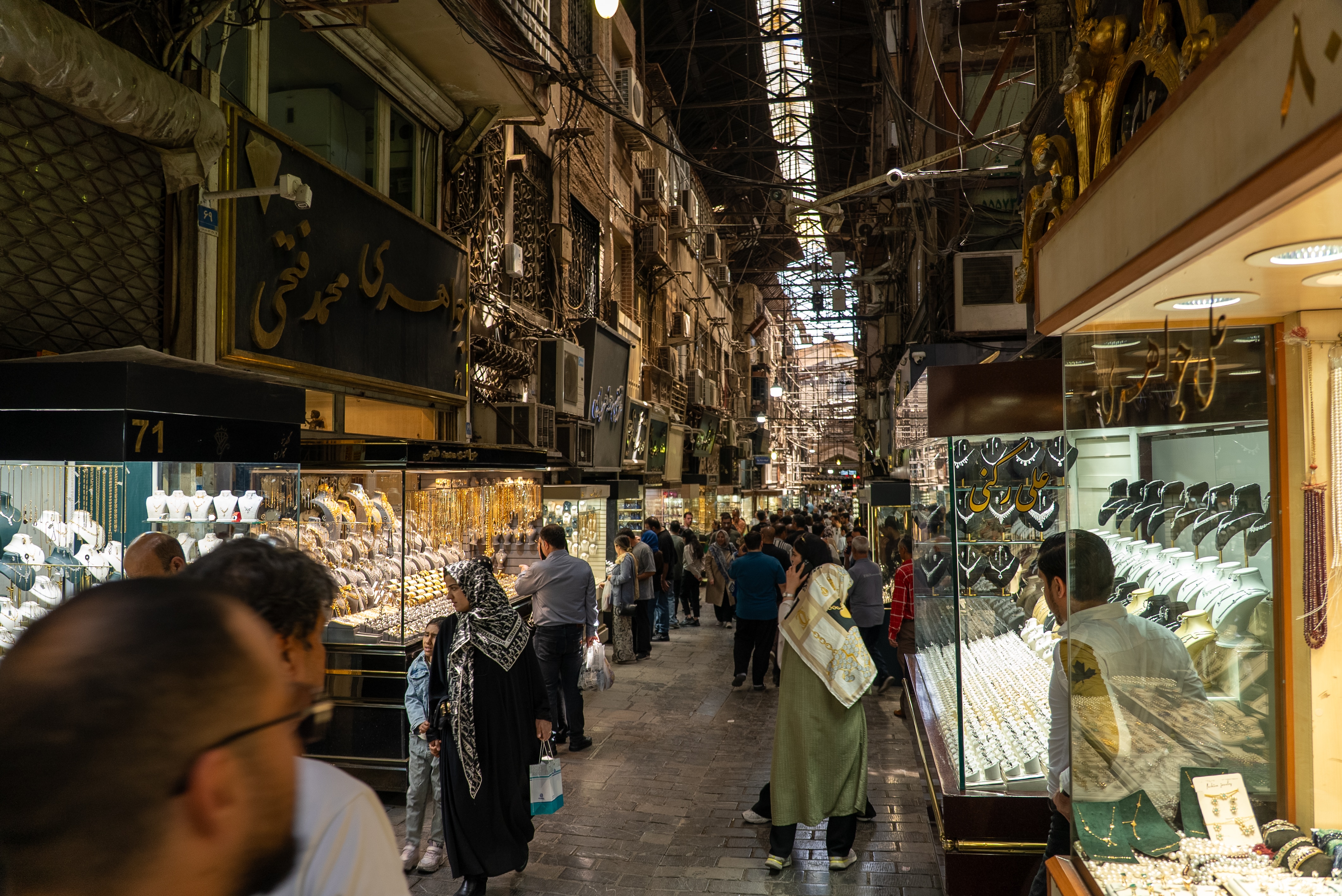 A narrow street with several jewllery merchants and people walking by.