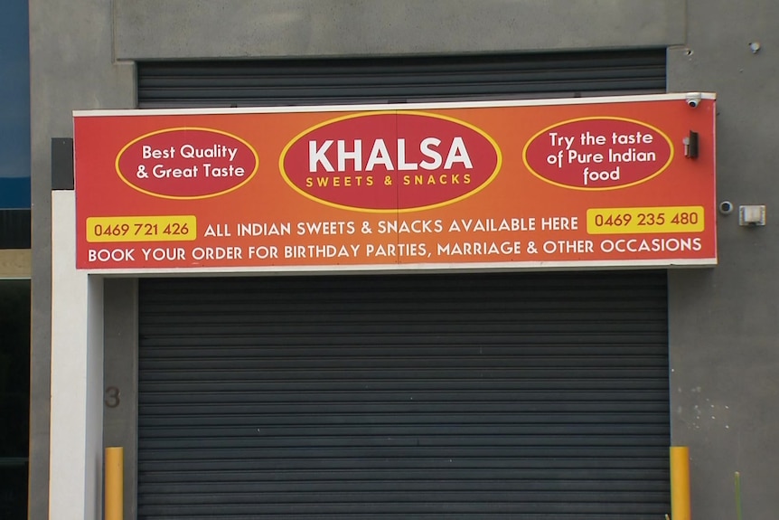 The orange sign of Khalsa Sweets & Snacks above a shuttered roller door.