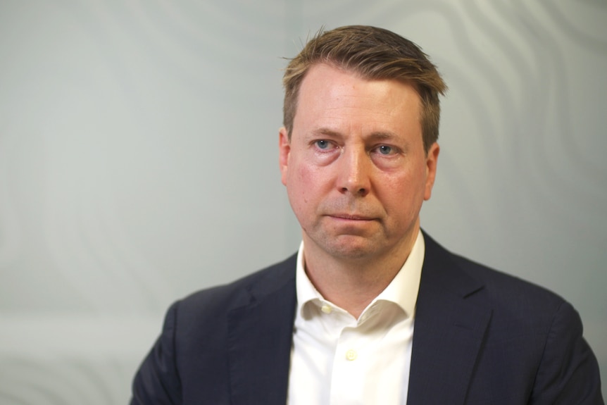 A man in a suit with fair skin and brown hair staring off camera