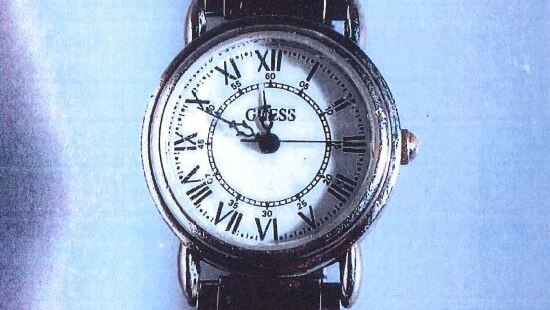 A close-up shot of a silver Guess watch with a white face lying on a blue surface.