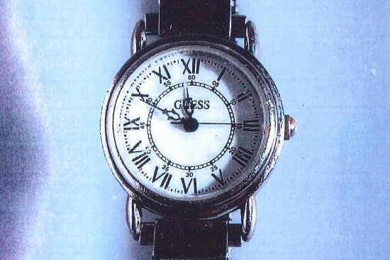 A close-up shot of a silver Guess watch with a white face lying on a blue surface.