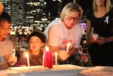 Rosie Batty holds a candle at a table near children who are also lighting candles, the lights of Brisbane CBD in the background