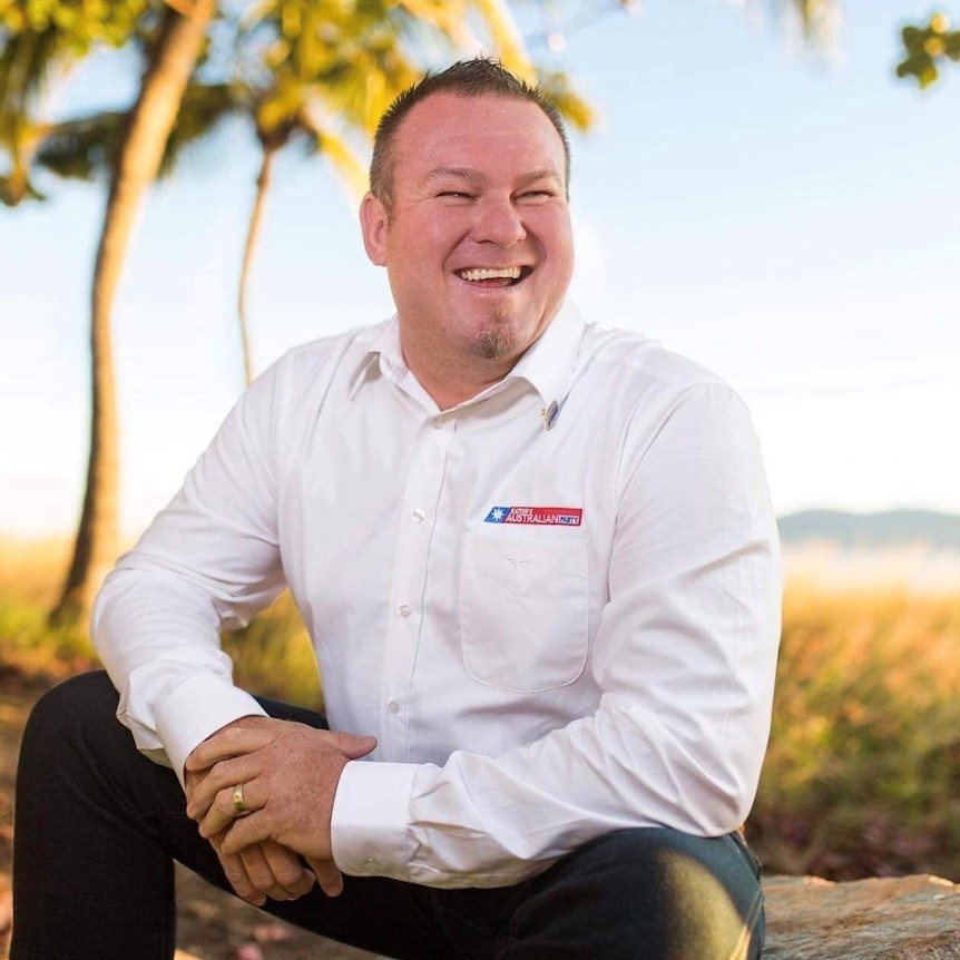 A man with a white dress shirt on smiles on a sunny day.