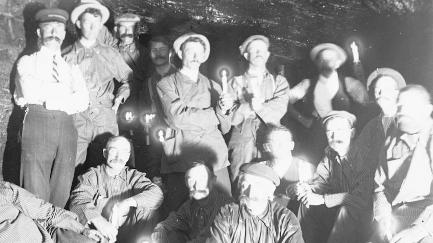 Black and white photo of mine workers inside a mine, some holding lit candles.