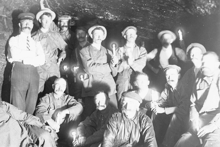 Black and white photo of mine workers inside a mine, some holding lit candles.